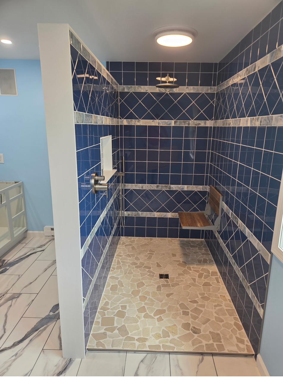 Curbless walk-in shower with navy diamond-pattern tile and a fold-down teak bench